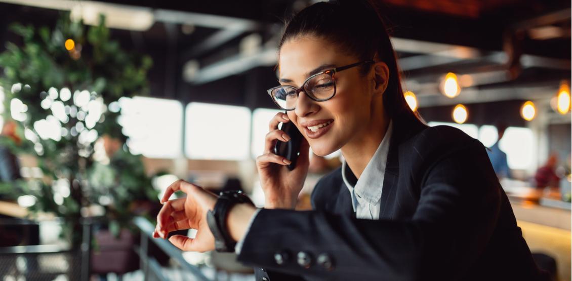 Professional woman checks time on her wrist watch while talking on the phone