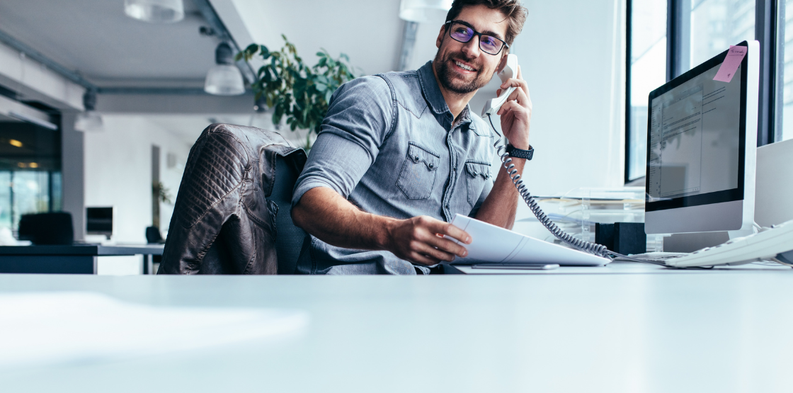 Man sitting at desk talking on the phone holding a stack of papers